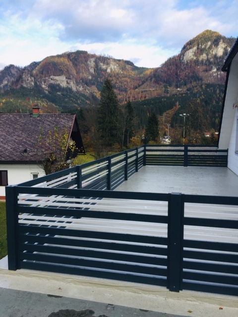 ein Haus mit schwarzem Zaun und Bergen im Hintergrund